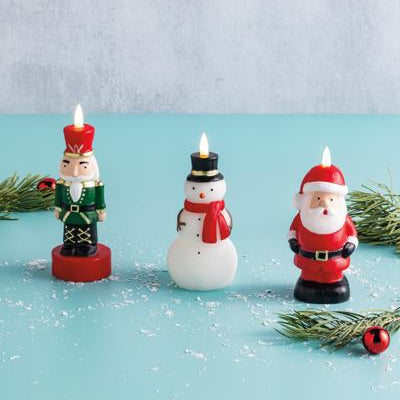 Three Christmas-themed candles on a blue surface with a light gray background