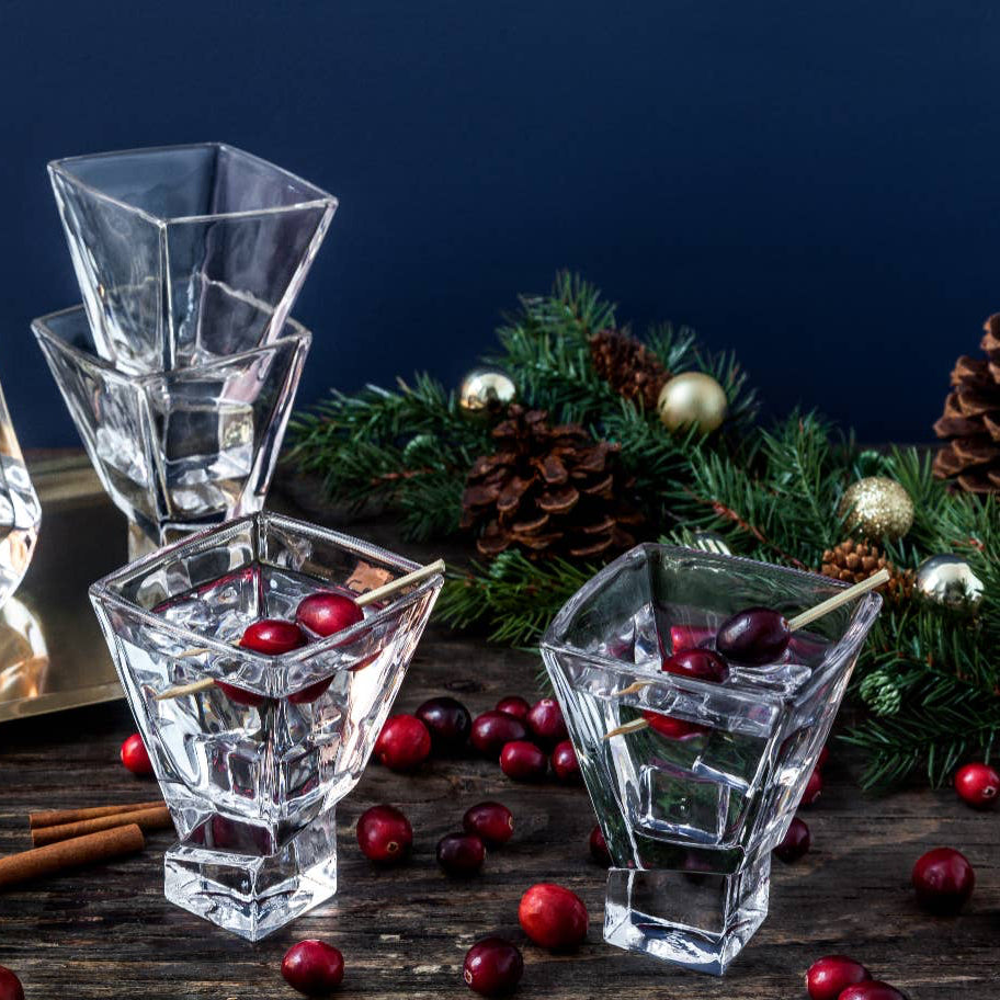 Clear glass decanter and glasses with cranberries on a wooden surface with Christmas decorations.
