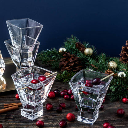 Clear glass decanter and glasses with cranberries on a wooden surface with Christmas decorations.