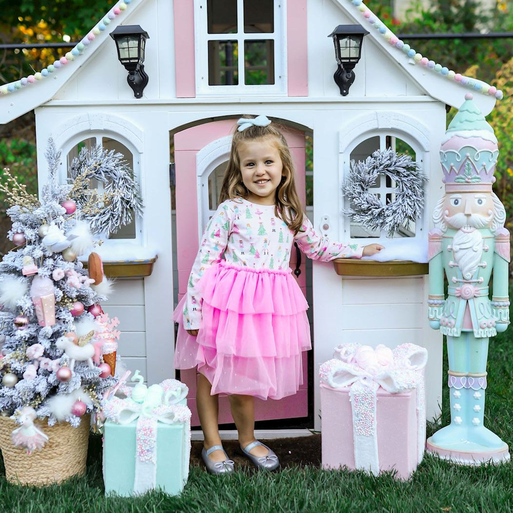 Young girl in a pink dress standing in front of a decorated playhouse with Christmas decorations.
