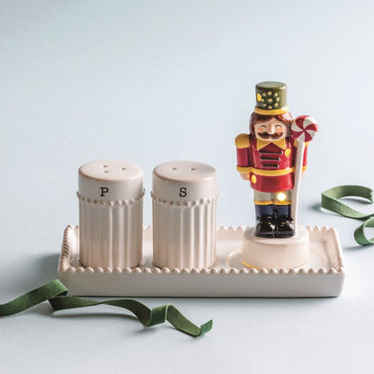 Salt and pepper shakers on a decorative stand with a nutcracker figure on a light gray background
