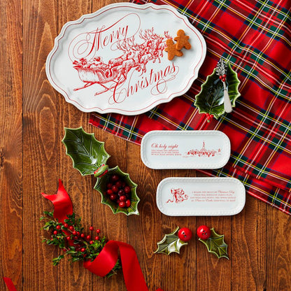 Christmas-themed place settings with holly leaves, ribbons, and plaid tablecloth on a wooden surface.