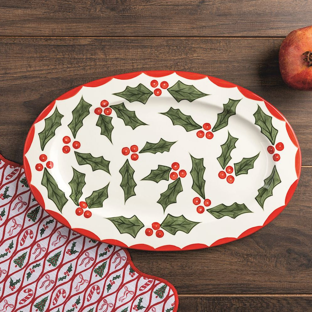 Decorative platter with holly design on a wooden surface with a pomegranate.