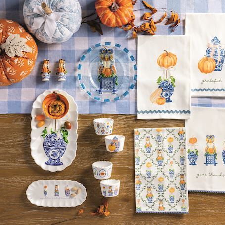 Table setting with decorative items, including pumpkins and patterned tableware, on a checkered tablecloth.