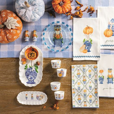 Table setting with decorative items, including pumpkins and patterned tableware, on a checkered tablecloth.