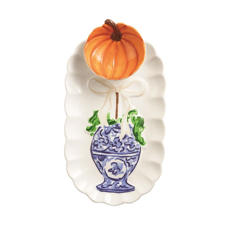 An autumn-themed ceramic serving platter featuring a white scalloped edge, a blue and white floral pot illustration, green leaves, and a small orange pumpkin decoration tied to the top with a white bow.