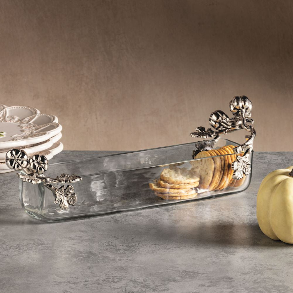 Decorative silver tray with floral handles on a gray surface with plates and a small pumpkin.