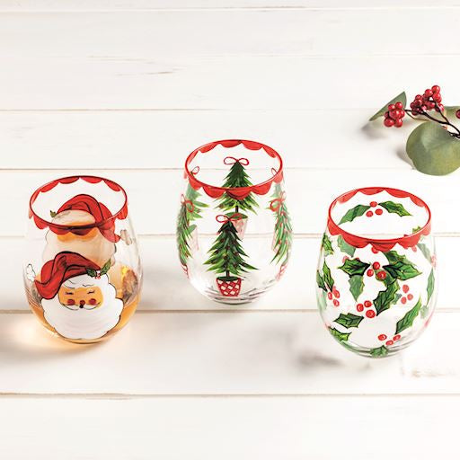 Set of three Christmas-themed stemless wine glasses on a white wooden surface.
