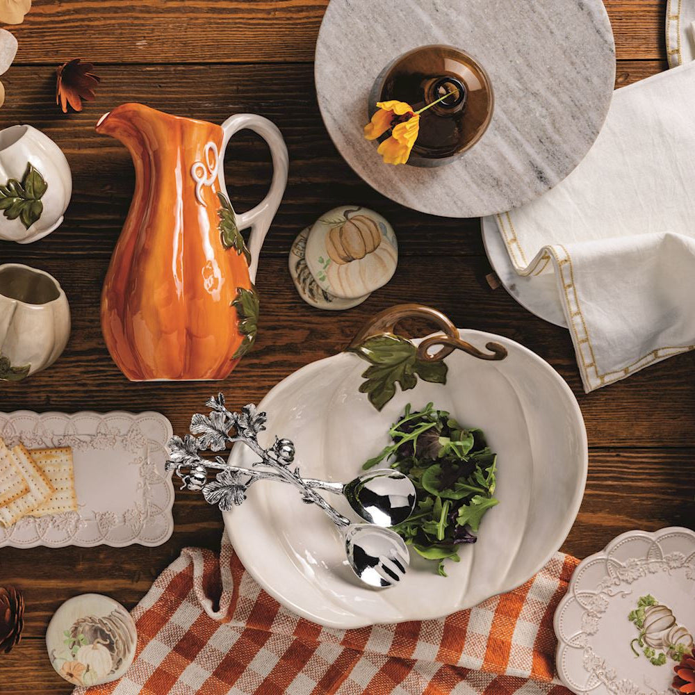 Dining table setting with ceramic pitcher, plates, and cutlery on a wooden surface.