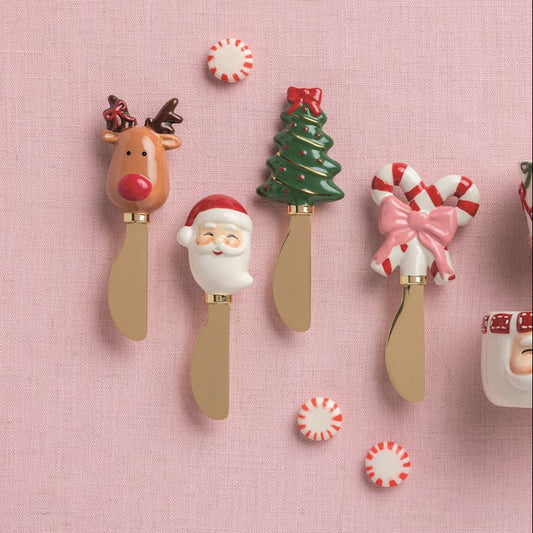 Set of Christmas-themed ceramic cups and spoons on a pink background
