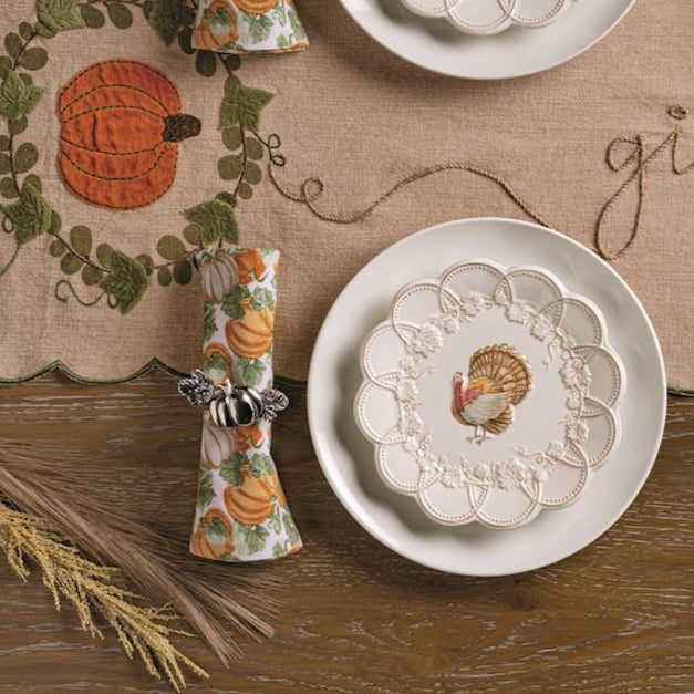 Thanksgiving table setting with pumpkins, place settings, and a 'give thanks' runner on a wooden table.