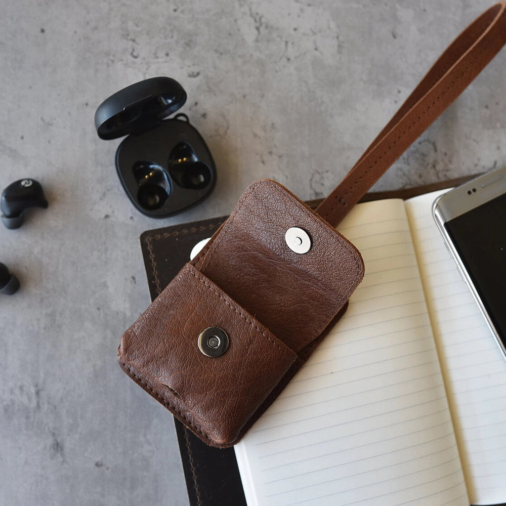 Brown leather case with wireless earbuds and smartphone on a gray surface