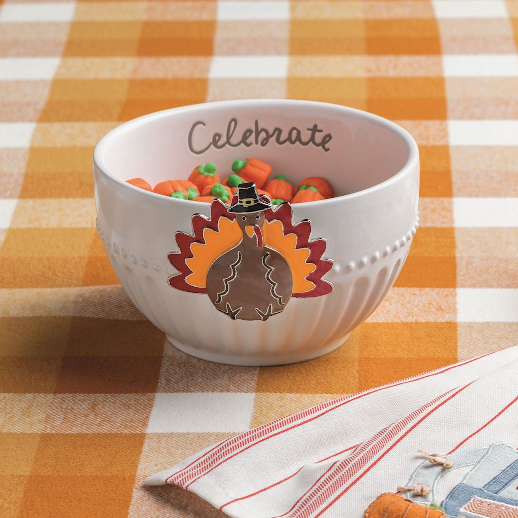 White bowl with a turkey design and 'Celebrate' text on a checkered tablecloth.
