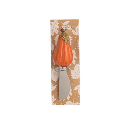A decorative kitchen knife with a sculpted orange pumpkin handle and green stem, mounted on a vertical kraft paper backing card with a white leaf pattern.