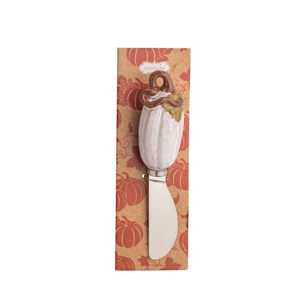 A decorative cheese knife with a white pumpkin-shaped handle and a wooden handle topper, presented on a vertical autumn-themed patterned backing card.