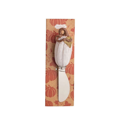 A decorative cheese knife with a white pumpkin-shaped handle and a wooden handle topper, presented on a vertical autumn-themed patterned backing card.