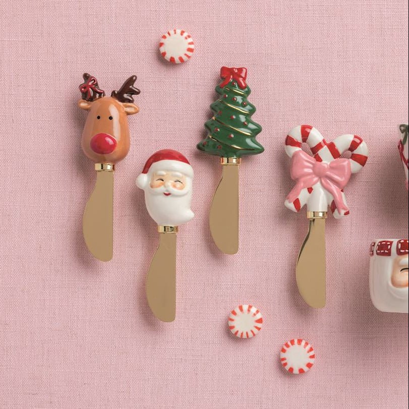 Set of Christmas-themed ceramic cups and spoons on a pink background