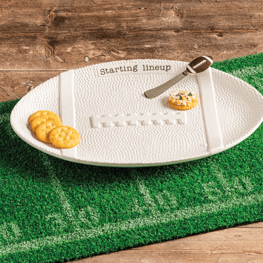 White football-shaped platter on a green field mat with snacks on a wooden surface