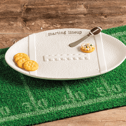 White football-shaped platter on a green field mat with snacks on a wooden surface