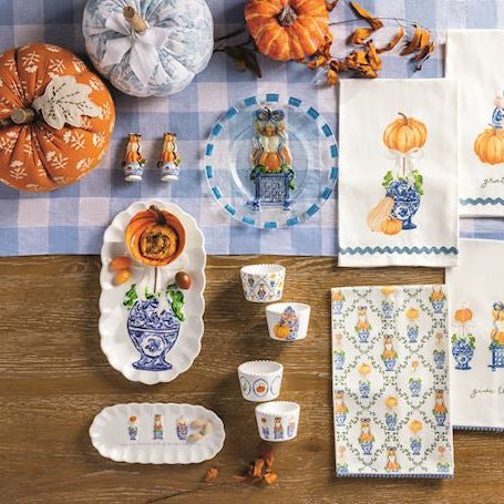 Table setting with decorative items, including pumpkins and patterned tableware, on a checkered tablecloth.
