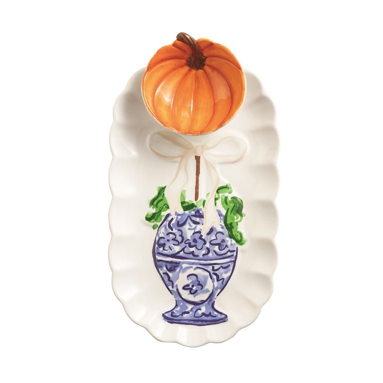 An autumn-themed ceramic serving platter featuring a white scalloped edge, a blue and white floral pot illustration, green leaves, and a small orange pumpkin decoration tied to the top with a white bow.