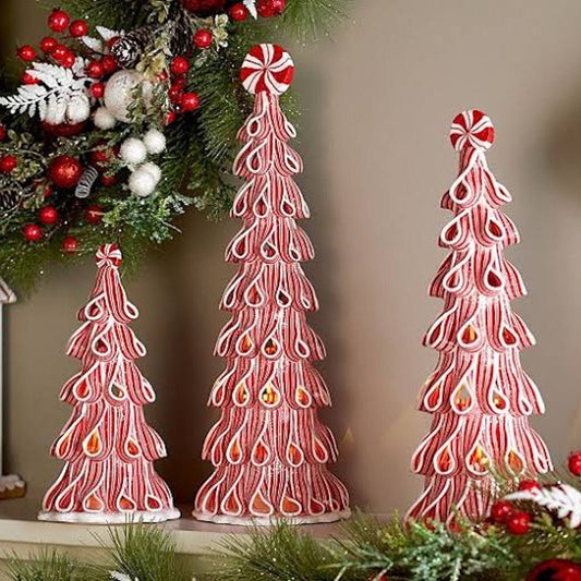 Three red and white candy cane Christmas tree ornaments of different sizes displayed on a shelf next to a decorated Christmas wreath.